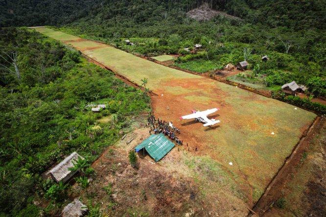 An aerial view of a grass airstrip in a forested area.