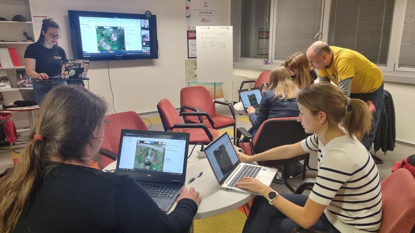 Six people in a small room are engrossed in their work on laptops. Visible on the screens are the OSM iD editor.